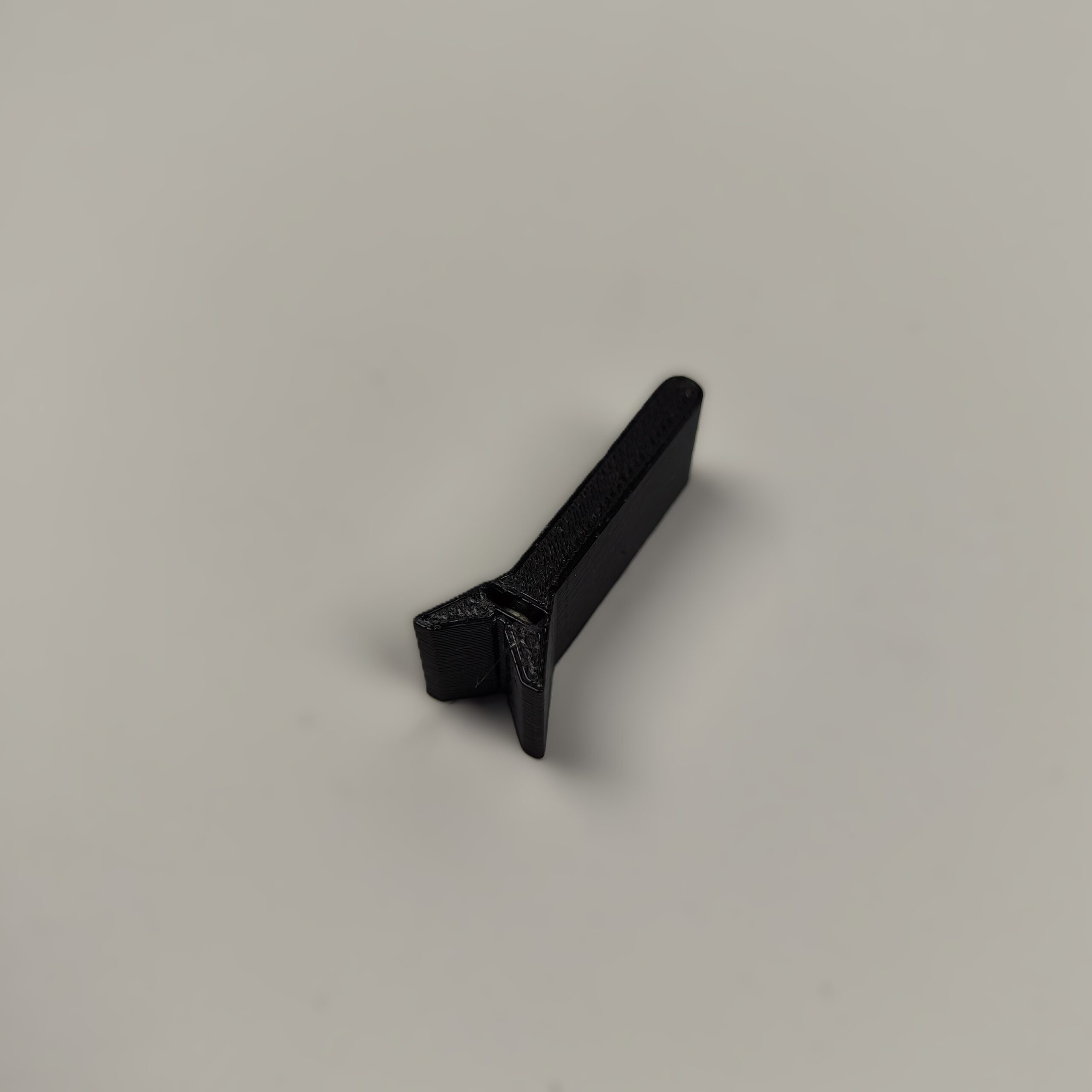 Magnetyczny uchwyt do gwoździ wykonany w technologii druku 3D z czarnego tworzywa, ułatwiający precyzyjne wbicie gwoździa bez narażania palców. Akcesorium ma formę płaskiego elementu z widocznym okrągłym zagłębieniem na magnes i szczeliną stabilizującą gwóźdź