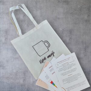 Biała materiałowa torba z grafiką kubka, z której wystają arkusze instrukcji „Przewodnik do pracy z torbą” oraz materiały edukacyjne o emocjach i arteterapii na szarym tle