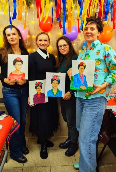 Cztery uśmiechnięte kobiety pozujące z ukończonymi obrazami Fridy Kahlo na płótnach podczas warsztatów w Warsztatowni, otoczone balonami i kolorowymi dekoracjami
