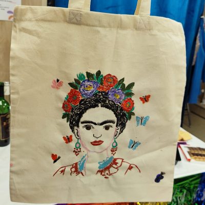 Bawełniana torba z ręcznie malowanym portretem artystycznym – bogata kwiatowa dekoracja, motyle i kolorowe detale na tle warsztatowego stołu