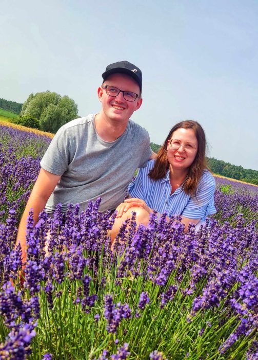 Uśmiechnięta młoda para siedzi pośród gęstych, fioletowych rzędów kwitnącej lawendy podczas słonecznego dnia