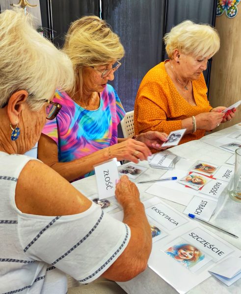 Zbliżenie na dłonie uczestniczek warsztatów układających karty z nazwami emocji, takimi jak Szczęście, Ekscytacja, Strach, Radość i Złość