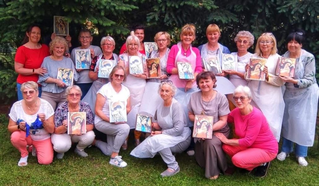 Duża grupa uśmiechniętych kobiet prezentuje gotowe obrazy ze złoceniami podczas warsztatów Warsztatowni w plenerze. Monika Wojdyło