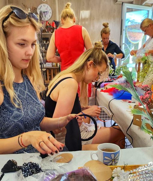 Młode kobiety w skupieniu tworzą rękodzieło podczas warsztatów DIY w Warsztatowni; na stole widać materiały plastyczne i herbatę