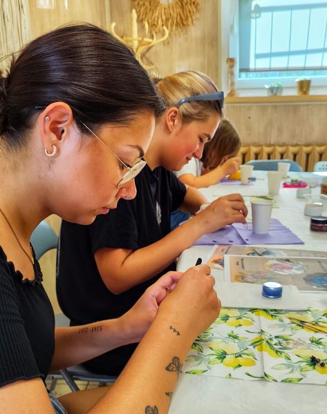 Młoda kobieta z tatuażami w skupieniu pracuje nad projektem decoupage z motywem cytryn podczas warsztatów w Warsztatowni