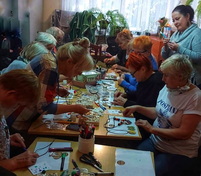 Liczna grupa kobiet w skupieniu tworzy biżuterię z koralików podczas warsztatów rękodzielniczych Warsztatowni w świetlicy. Monika Wojdyło