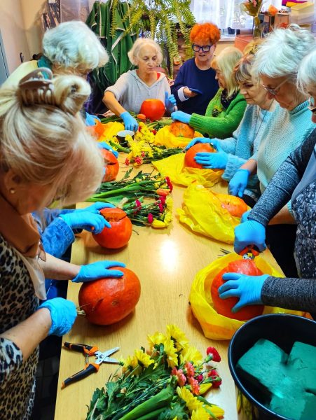 Grupa kobiet w skupieniu przygotowuje dekoracje kwiatowe w dyniach podczas warsztatów florystycznych Warsztatowni