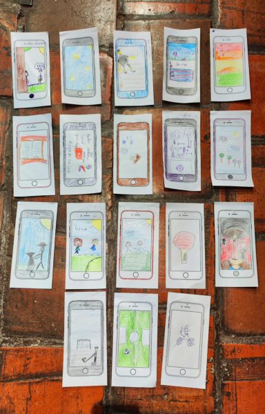 Zbiór osiemnastu rysunków dzieci wykonanych na szablonach papierowych smartfonów, ułożonych na ceglanej podłodze. Rysunki przedstawiają różne sceny: od słońca i przyrody, przez sport, aż po czytanie książek i relacje z bliskimi