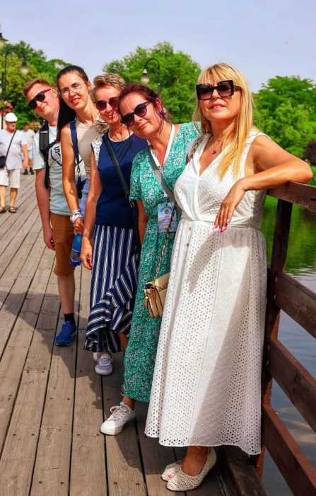 Grupa pięciu uśmiechniętych osób, w tym Monika Wojdyło w zielonej sukience, pozuje na drewnianym pomoście nad jeziorem w Inowrocławiu w słoneczny dzień