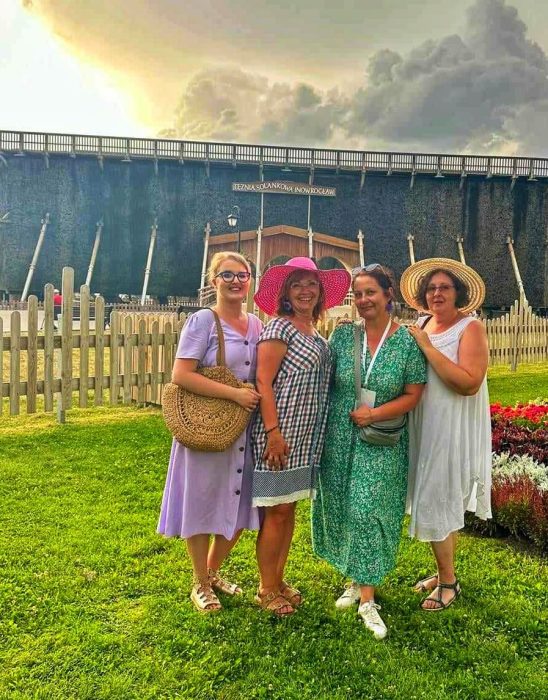Cztery uśmiechnięte kobiet, w tym Monika Wojdyło w zielonej sukience, pozuje na tle drewnianej tężni solankowej w Inowrocławiu w słoneczny dzień